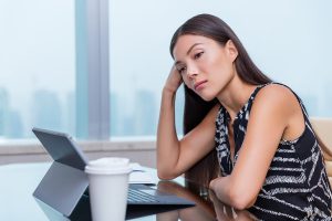 Bored or sad woman working at office job. Negative work concept. Tired businesswoman sitting at desk in front of laptop thinking about problems and showing dissatisfaction of career.